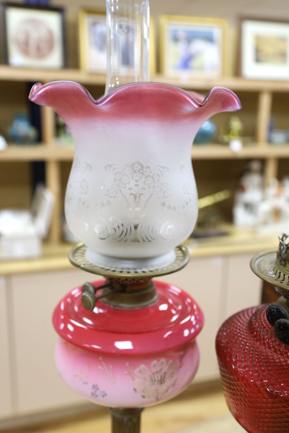 A brass column oil lamp with cranberry glass reservoir and frilled frosted and pink glass shade and a similar oil lamp